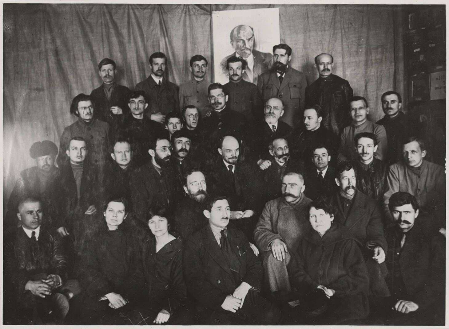 Czarno-biała fotografia przedstawia pamiątkowy portret zbiorowy we wnętrzu. W centrum grupy, w drugim rzędzie, pozuje osobiście Włodzimierz Lenin w otoczeniu wielu mężczyzn i trzech kobiet. Postacie ustawione są w czterech rzędach na tle udrapowanej tkaniny. W jej centrum i u góry kadru widnieje portret Lenina. Kobiety siedzą w pierwszym rzędzie. 