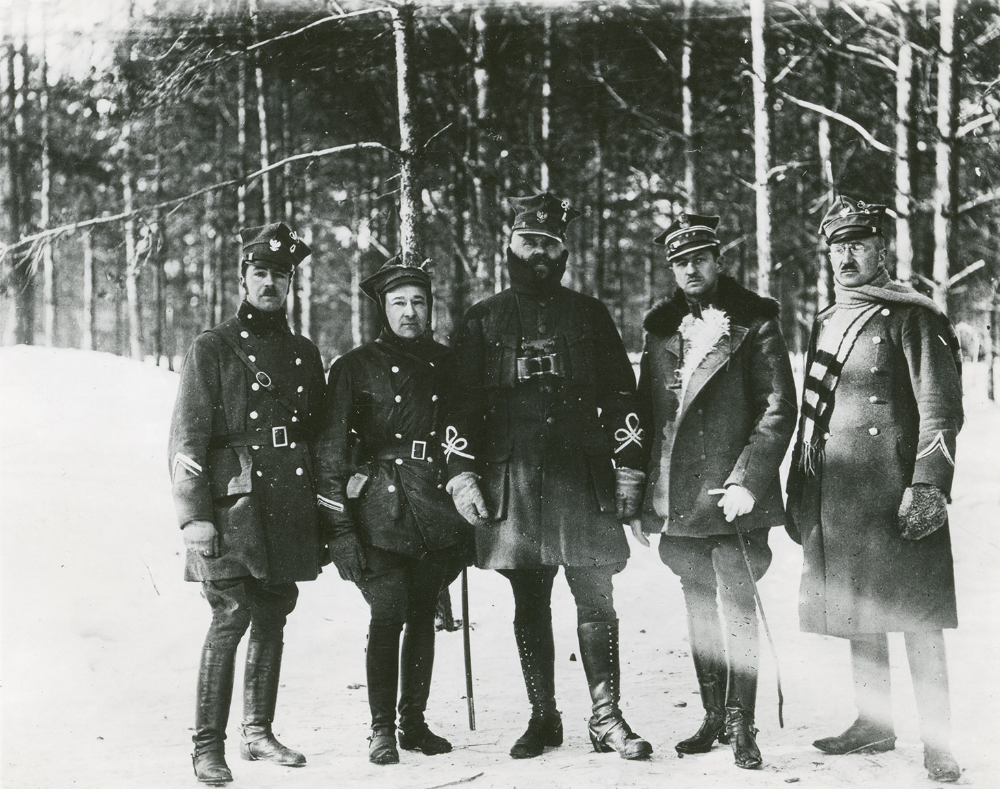 Czarno-biała fotografia przedstawiająca grupę pięciu oficerów w mundurach na tle zimowego lasu. Od lewej stoją: dwaj żołnierze w kurtkach zimowych, dwurzędowych i butach oficerkach. Trzecia postać centralna i najwyższa to Generał Daniel Konarzewski. Stoi z opuszczonymi swobodnie rękami w kurtce z oznakami generalskimi na rękawach, w bryczesach i wysokich butach . Na jego szyi zawieszona jest lornetka. Żołnierz stojący czwarty od lewej pozuje ze szpicrutą w ręku. Piąty i ostatni w rzędzie oficer ubrany jest w dwurzędowy płaszcz wojskowy, wokół szyi zarzucony ma długi jasny szal. Na głowach wszystkich mężczyzn czapki rogatywki.